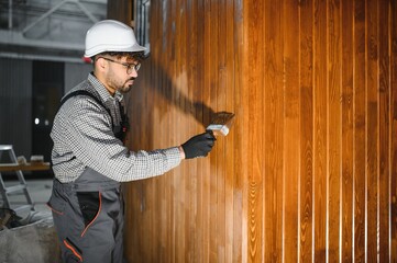 Construction worker applying varnish on wooden wall in workshop