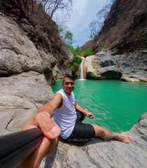 Young man taking a selfie near a waterfall in a rocky canyon
