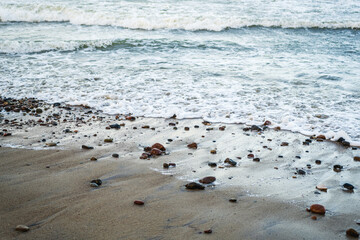 Waves softly roll onto a sandy beach scattered with smooth pebbles capturing the early morning light The shoreline creates a serene atmosphere perfect for reflection