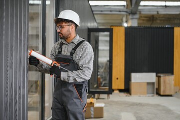 Construction worker applying sealant to modular house wall in workshop