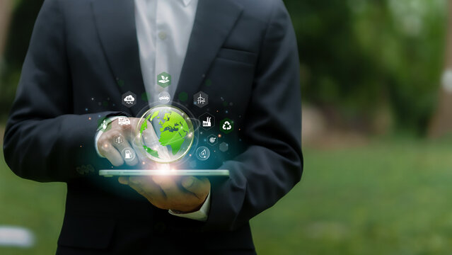 Green Business Sustainble Innovation concept. Businessman holds a tablet projecting a green Earth surrounded by eco-related icons, symbolizing sustainability and green technology. Renewable energy.