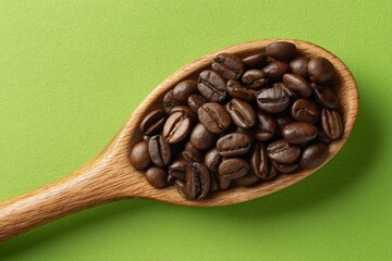Fototapeta premium Wooden spoon filled with dark roasted coffee beans on a bright green background