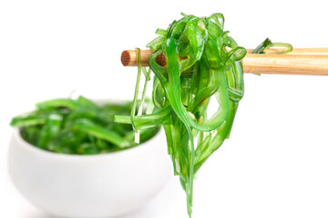 Chopsticks holding Japanese seaweed salad. Japanese cuisine - Wakame salad, Chuka seaweed salad isolated on a white background.