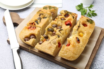 Cut delicious focaccia with flowers made of vegetables and knife on light grey table, closeup