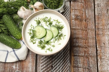 Tasty cucumber soup in bowl and ingredients on wooden table, flat lay. Space for text