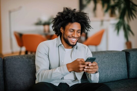 Smiling african male adult texting on smartphone in modern living room