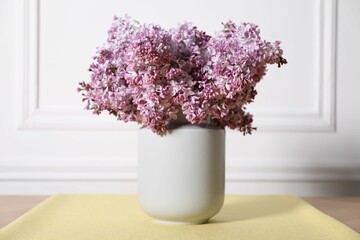 Beautiful lilac flowers in vase on table near white wall indoors
