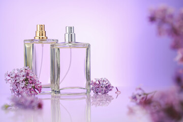 Bottles of perfume and lilac flowers on mirror surface against violet gradient background,...