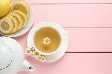 Delicious chamomile tea in cup, fresh flowers and lemon on pink wooden table, flat lay. Space for text