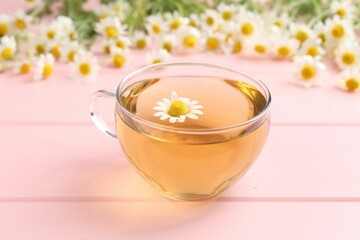 Delicious chamomile tea in glass cup and fresh flowers on pink wooden table, closeup