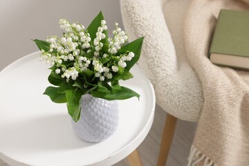 Bouquet of beautiful lily-of-the-valley in vase on coffee table near armchair indoors