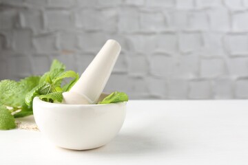Fresh lemon balm leaves and pestle in mortar on white wooden table. Space for text