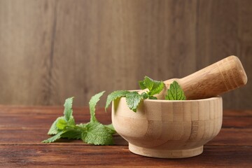 Fresh lemon balm leaves, pestle and mortar on wooden table, closeup