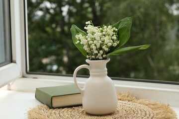 Bouquet of lily-of-the-valley flowers in vase and book on windowsill indoors