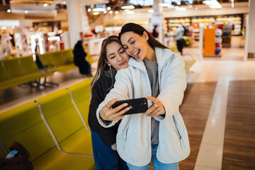 Two female friends are posing and smiling while looking at the phone one of them is holding