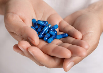 Cupped female hands with a pile of blue medical herbal capsules closeup over white shirt