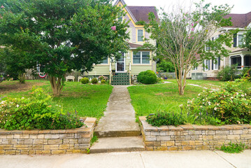 classic American house with stone pavement leading to the front door. Flowers, lawn and trees in front of the entrance.