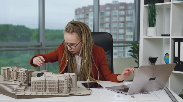 Woman designer with dreadlocks working on computer on construction project sketch in architectural bureau