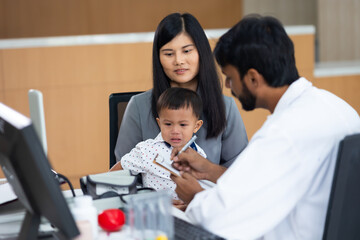 pediatrician : Indian male Doctor working with little asian boy patient and family at hospital and wellness center.