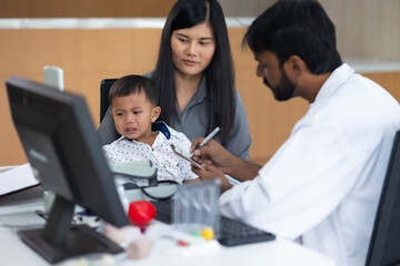 pediatrician : Indian male Doctor working with little asian boy patient and family at hospital and wellness center.