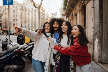 A group of four female friends stand and look in surprise in the direction one of them is pointing, on the street