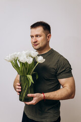 A manly guy in a green t-shirt holds a bouquet of white tulips and congratulates the girls