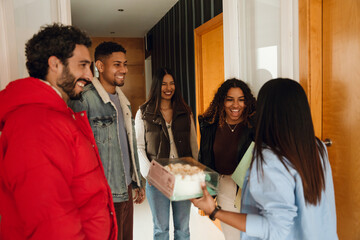 A group of four friends stand and smile while looking at a female friend standing next to them...