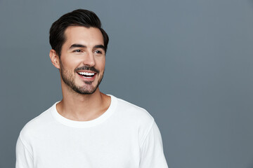 Smiling young man wearing a casual white t-shirt looks camera with a charming smile on a simple...