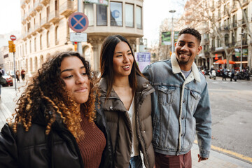 Fototapeta premium Group of three friends walking and smiling while talking, outdoors