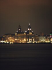 Naklejka premium A captivating night-time photograph of Liverpool's most iconic landmark — the Royal Liver Building. Its glowing clock faces and architectural elegance reflect against the calm waters of the Mersey.