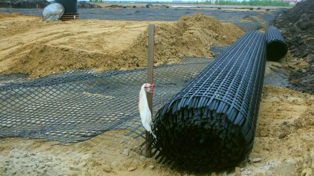 Installing a geogrid on construction site, preparing the ground for asphalt paving, enhancing stability and preventing future road damage. Geogrid installation for road construction and reinforcement