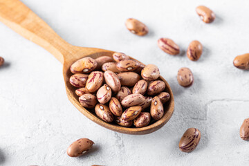 Borlotti beans on a wooden spoon on a gray table surface. Popular in Mediterranean diets, these legumes are rich in fiber and protein, often used in soups and stews