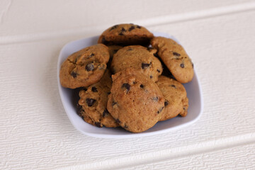 Chocolate chip cookies in a white bowl on white table background, copy space. Close up photo. Front view.