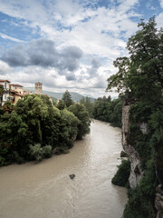 The muddy Natisone River winding between lush green cliffs and medieval buildings under a dramatic cloudy sky in Cividale.