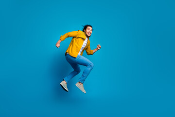 Fototapeta premium Energetic young man jumping joyfully in stylish casual outfit against vivid blue background celebrating happiness