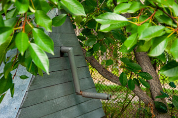 Water well view through garden tree leaves, selective focus. Rural water supply. Garden serenity. Countryside charm. Quiet countryside moment in summer. Village technology. Rusty well handle