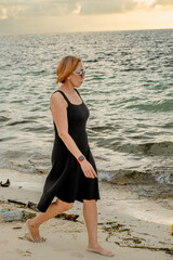 A very beautiful woman with shoulder-length blonde hair and sunglasses was enjoying an afternoon at the beach. Walking along the beach with beautiful white sand.