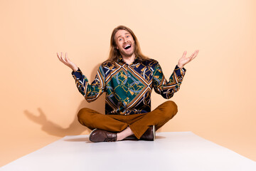 Charismatic stylish man with long hair showing expressive hand gestures while sitting cross legged...