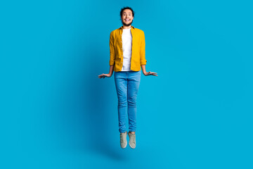 Cheerful young man wearing a yellow shirt on a vibrant blue background jumping in joy and excitement