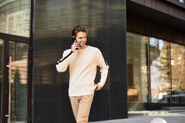 Handsome man smiling while walking and talking on the phone in a modern city setting