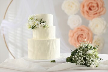Delicious wedding cake with floral decor and bouquet on table indoors