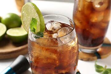 Tasty Cuba Libre cocktail in glasses, ingredients and muddler on white table, closeup