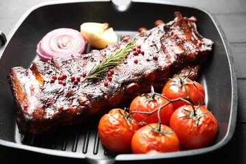 Delicious roasted pork ribs with rosemary, tomatoes and onions on grey wooden table, closeup