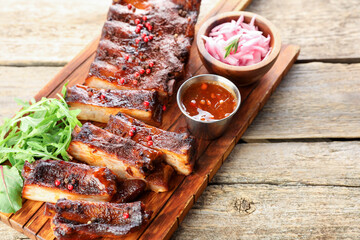 Delicious spare ribs, onion, sauce and arugula on wooden table