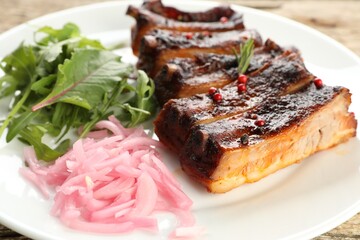 Delicious spare ribs, onion and arugula on wooden table, closeup