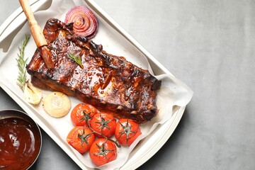 Delicious spare ribs, rosemary, baked onion, sauce and sun dried tomatoes on grey table, flat lay. Space for text