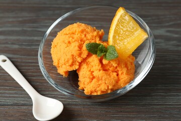 Balls of tasty orange sorbet, fresh fruit, mint and spoon on wooden table, closeup