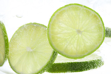 Refreshing soda water with slices of lime in glass on white background, closeup
