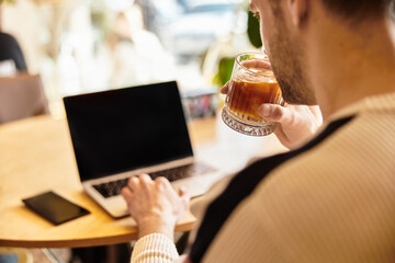 Handsome man enjoying a drink while working on his laptop in a cozy cafe atmosphere