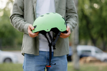 Individual holds a green helmet in a park surrounded by trees and parked vehicles during daylight...